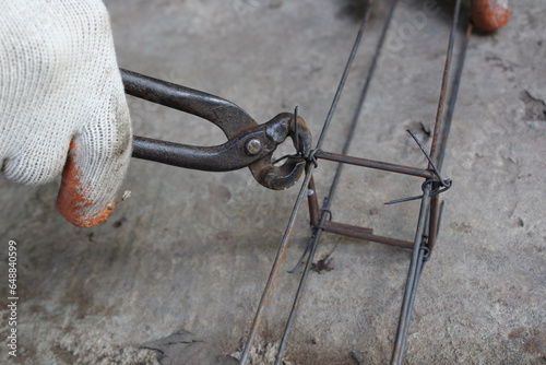 Workers hands using steel wire and pincers to secure rebar before concrete is poured over it