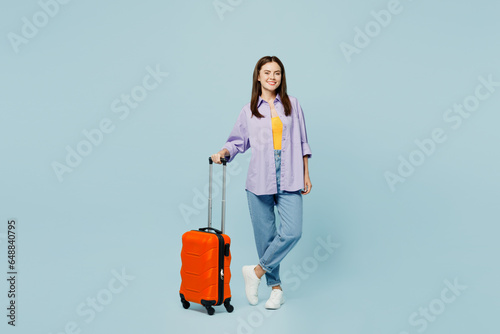 Traveler happy woman wear casual clothes hold suitcase bag look camera isolated on plain pastel blue background. Tourist travel abroad in free spare time rest getaway. Air flight trip journey concept. photo