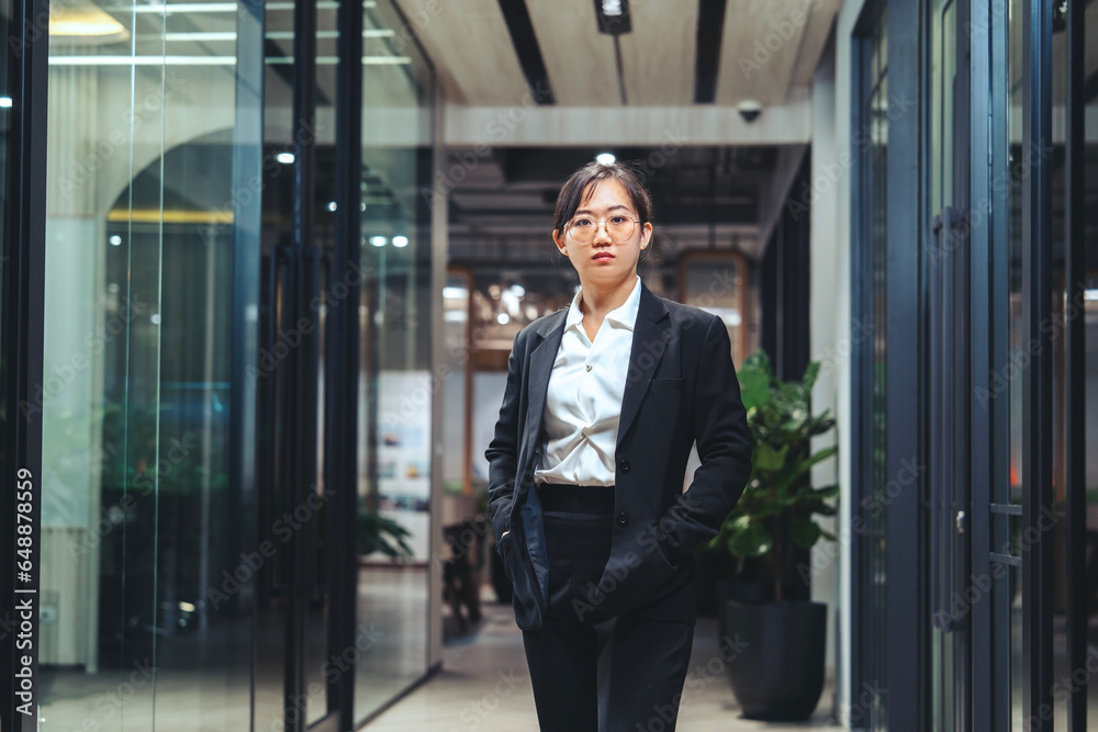 Young Asian woman wearing glasses, wearing a black suit, professional executive, standing confident in work success, standing in front of a company conference room. Young Asian woman wearing glasses, wearing a black suit, professional executive, standing confident in work success, standing in front of a company conference room.