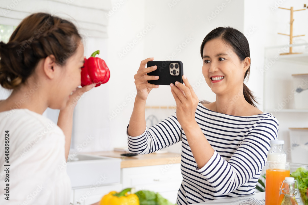 Happy two woman friends shooting video with mobile phone to share online while cooking in kitchen at home Happy two woman friends shooting video with mobile phone to share online while cooking in kitchen at home