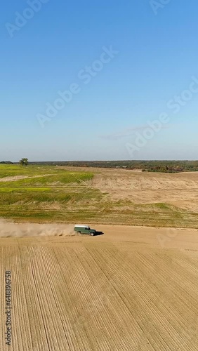 Vertical video. A green SUV with a white roof is driving on a dirt road between two fields at high speed. There was dust behind the car. Aerial view. photo