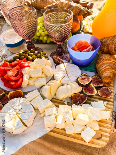 festive party setting with variety of cheeses, olives, poidos, grapes, croissants, figs and glasses of wine on the beach. valentine's day picnic with cheeses and fruits on the beach