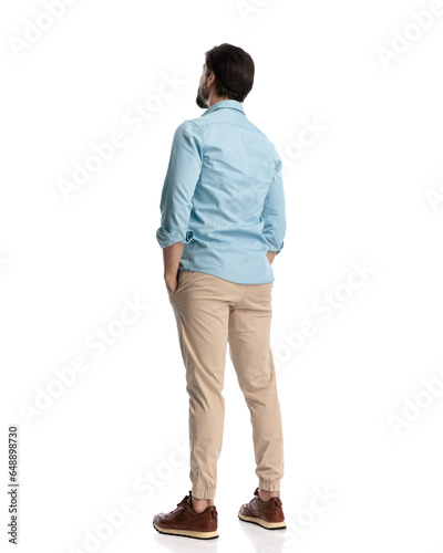 back view of young casual man holding hands in pockets and standing