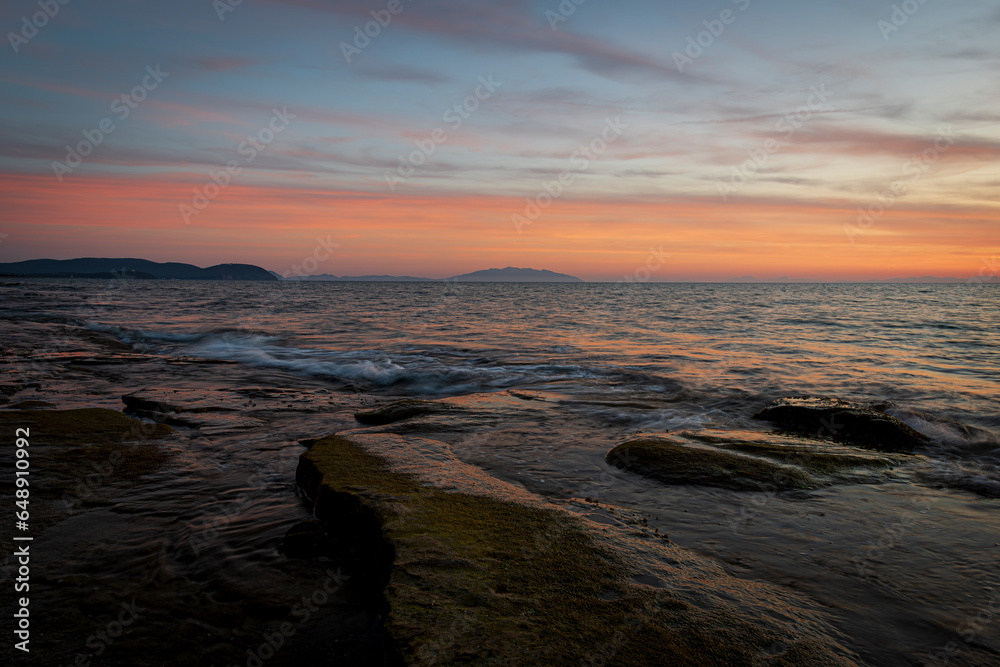 View of Elba island from Tuscany coast with flat rocks in the foreground