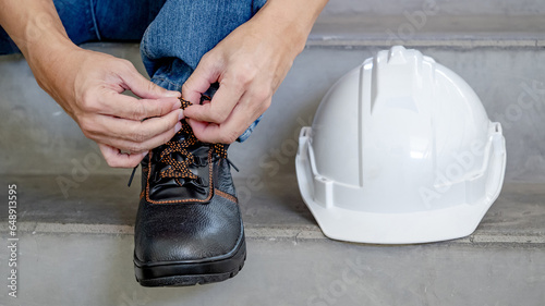 Εκτύπωση καμβά Male worker hands tying shoelaces on leather safety shoes with white protective helmet or hard hat on concrete stair in construction site
