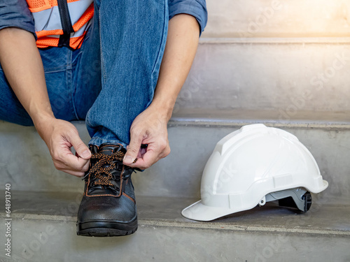 Male worker hands tying shoelaces on leather safety shoes with white protective helmet or hard hat on concrete stair in construction site. Safety workwear for worker and foreman photo