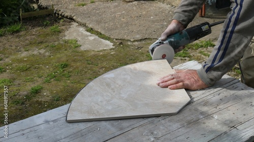 sanding the edge of a large decorative light tile in an outdoor workshop using a round sanding attachment, processing building finishing material with an angle saw with sandpaper