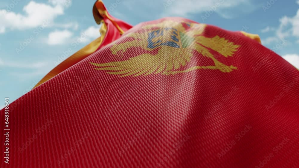 Wavy flag of Montenegro blowing in the wind in slow motion. Waving official Montenegro flag team symbol abstract vertical background. Blue sky with clouds. World countries flying flags concept
