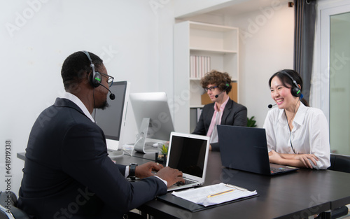 Group of business people wearing headset working actively in office. Call center, telemarketing, customer support agent provide service on telephone video conference call. © Wosunan