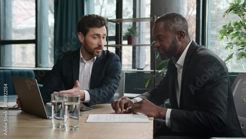 Diverse multiracial African American and Caucasian men colleagues coworkers businessmen financial agents discuss business project startup with laptop in office work with papers documents paperwork