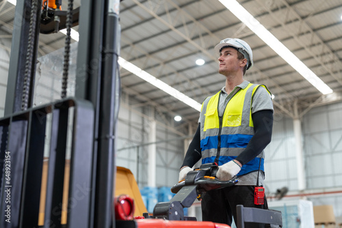 Obraz na plátně Man worker driver using forklift electric or electric pallet stacker lift moving cardboard boxes sheet goods in paper box factory