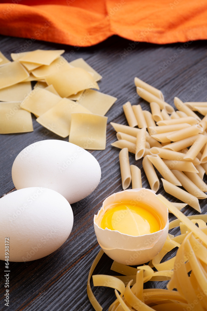 variety of types and shapes of italian pasta on dark wooden table with ingredients, flour and eggs. dry pasta background. close up