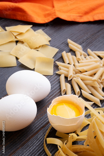 variety of types and shapes of italian pasta on dark wooden table with ingredients, flour and eggs. dry pasta background. close up photo