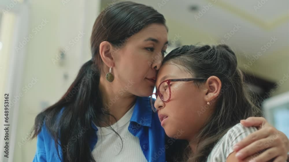 Medium close up of woman supporting and cuddling her teenage daughter while waiting for appointment in clinic