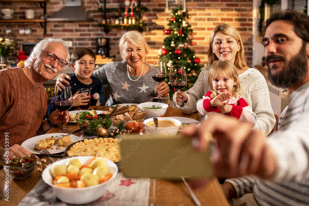 Multigenerational Caucasian family taking a selfie on smartphone while eating dinner at home during Christmas and the new year holidays