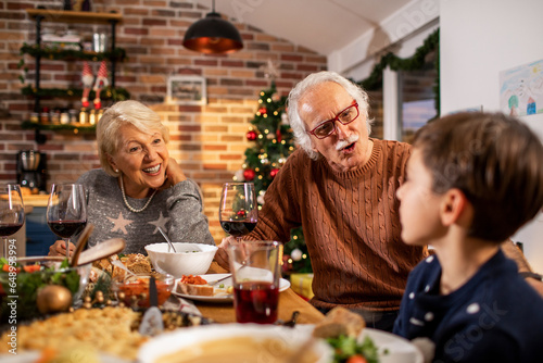 Grandparents having wine and dinner while having a conversation with their grandson at home during christmas and the new year holidays