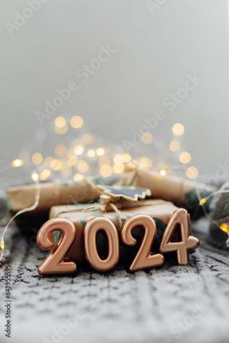Christmas and New Year Greeting Card. Number 2024 on knitted background. Holiday lights bokeh background. Happy New Year 2024 Concept.