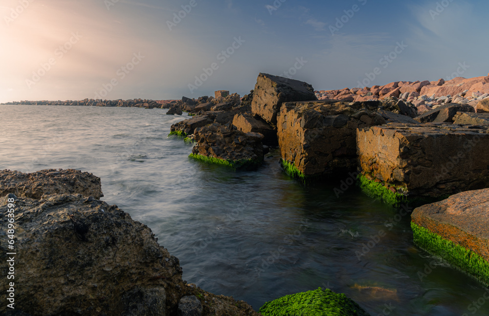A stone jetty in the evening sunlight. Background with sea and stone ridges