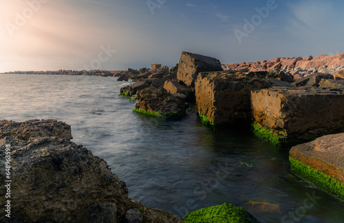 A stone jetty in the evening sunlight. Background with sea and stone ridges