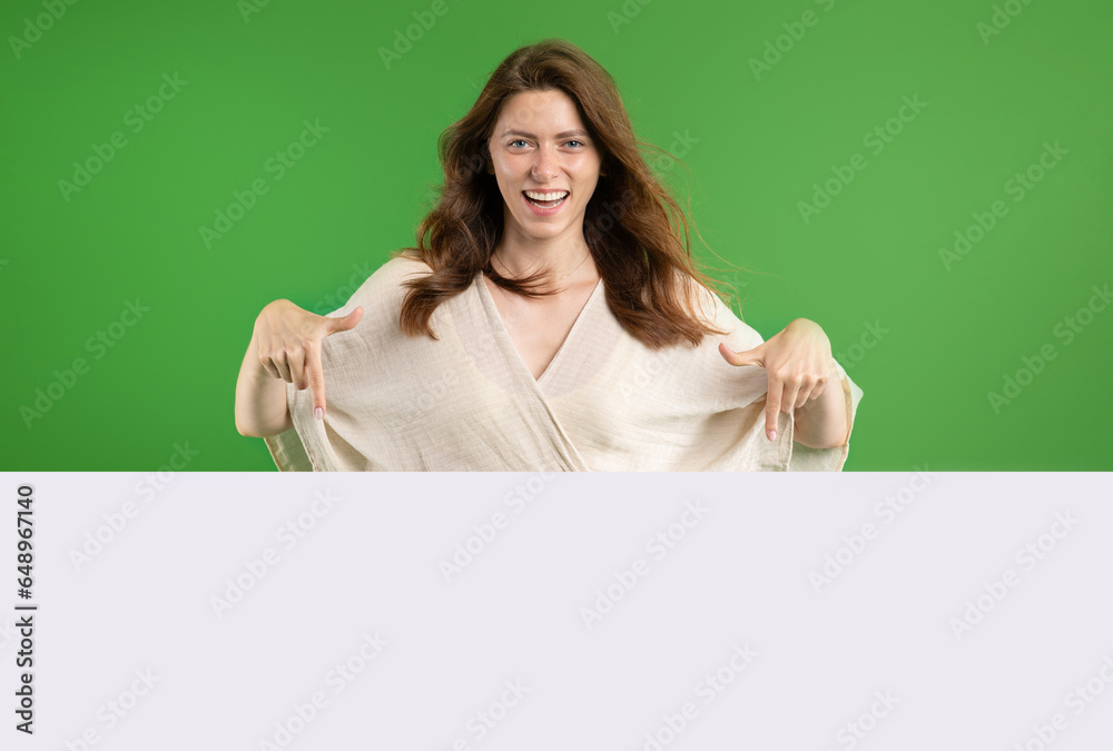 Smiling pretty young european lady in casual pointing fingers at large banner with empty space Smiling pretty young european lady in casual pointing fingers at large banner with empty space