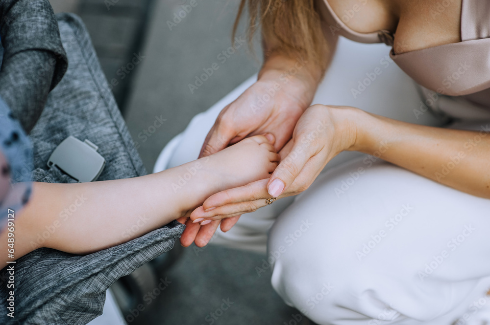Fototapeta premium Mother, an adult woman with her hands holds the leg of her little child, sitting in a baby carriage. Photography, portrait.