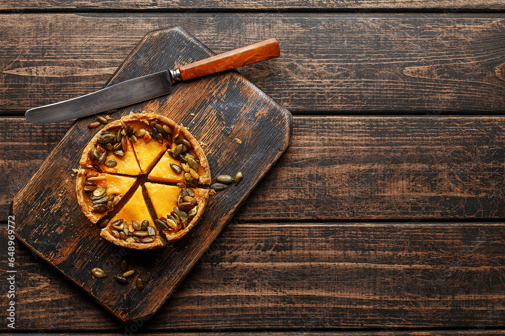 Colorful mini pumpkin tart decorated with roasted pumpkin seeds on rustic wooden board with vintage knife. Overhead view, copy space