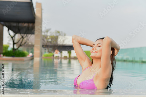 Asian woman in swimsuit emerging from pool. She is playing in the water having fun.