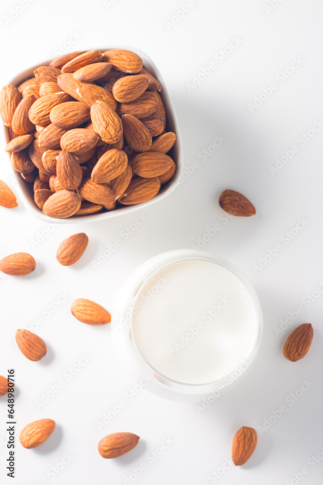 Organic almond milk in glass with raw almonds on white table Organic almond milk in glass with raw almonds on white table
