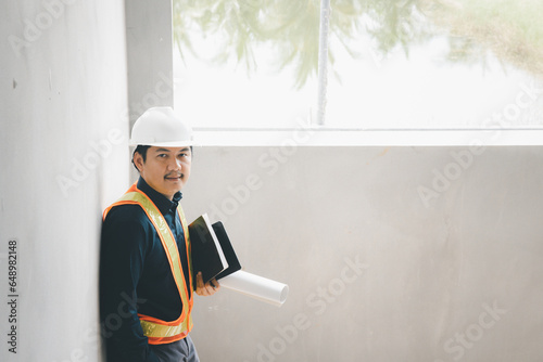 A foreman wearing a hard hat stands holding a blueprint. Supervising and inspecting the construction project of the building to be successful as planned.