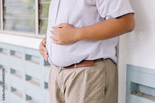 Thai students who are overweight, Thai children stand with their hands on their stomachs, school uniforms for fat children, the concept of fat students hungry for food.