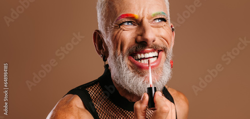 Obraz na płótnie Happy mature gay man with rainbow colored eyebrows applying lipstick against bro