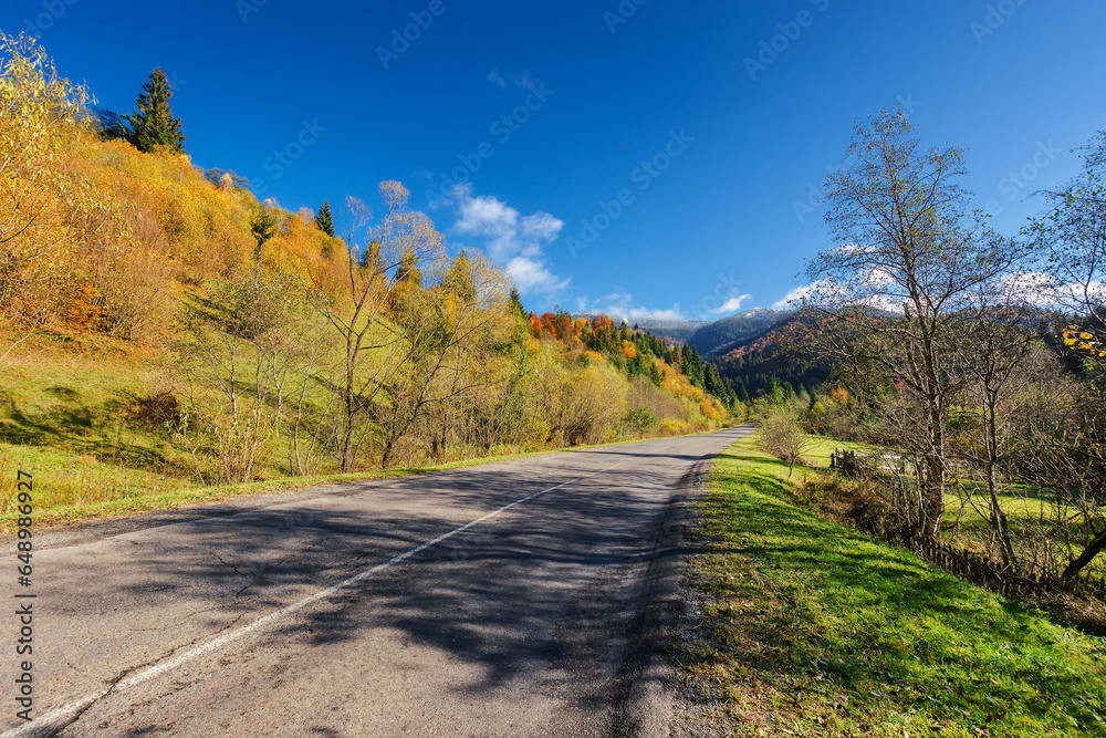 Obraz premium old asphalt road through countryside landscape in autumn. scenery with trees on the hill in colorful foliage. clouds on the blue sky above the distant forested mountain