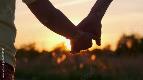 Mom and child holding hands together on sunset time. Silhouette as kids takes mother hand. close up