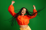 Happy young woman with dreadlocs dancing and smiling against green background