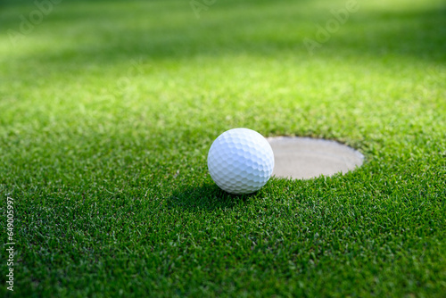 Closeup of white golf ball next to the cup on a putting green 