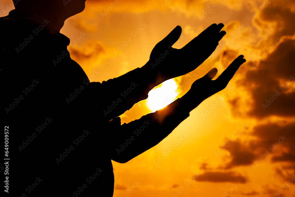 An inspiring photograph showing the silhouette of a man, his arms outstretched towards the breathtaking sunset of the solstice, immersed in heartfelt prayer.
