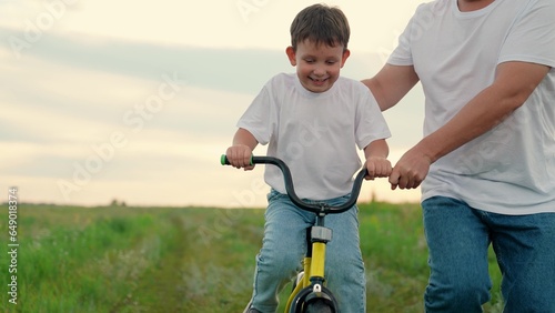 Childhood boy dream to ride bike. Dad teaches her little son to ride bicycle, sunset. Young father teaches child to keep balance while sitting on bicycle. Holiday family. Dad baby, Parental support