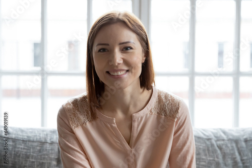 Headshot portrait of smiling millennial female sit on couch at home speak talk on video call, happy young Caucasian woman have webcam conversation or interview on gadget, technology concept