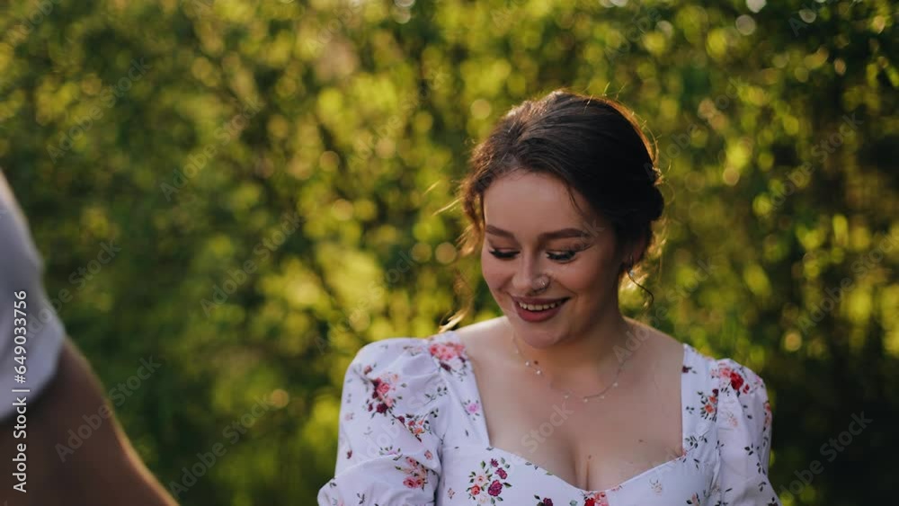 A very cute girl walks holding her boyfriend's hand and smiles coolly at him. They are walking in the evening park A very cute girl walks holding her boyfriend's hand and smiles coolly at him. They are walking in the evening park