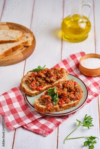 Two sandwiches with eggplant caviar made from baked eggplants, sweet peppers and tomatoes, seasoned with vegetable oil, on a green clay plate on a white wooden background.