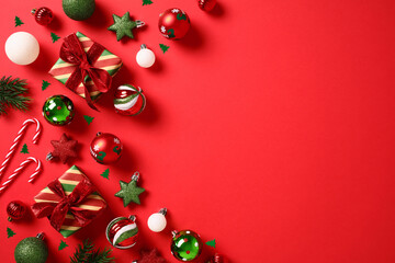 Red and green Christmas decorations, balls, gift boxes, candy canes, confetti, stars on red background. Christmas greeting card template, banner design. Flat lay, top view, copy space.