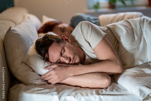 Man and woman sleep soundly well. Guy and girl dozing on same bed on soft regular comfortable pillows under warm blankets in glow of lights. Importance of long, healthy sleep. Joint sleep of spouses photo