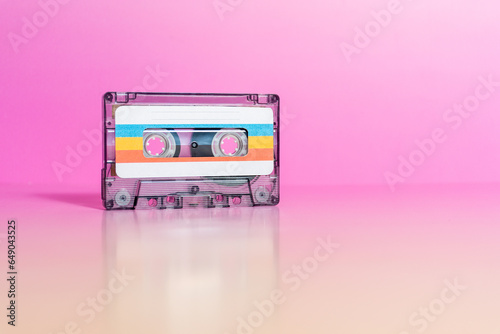 Transparent audio cassette with labels on fuchsia background.