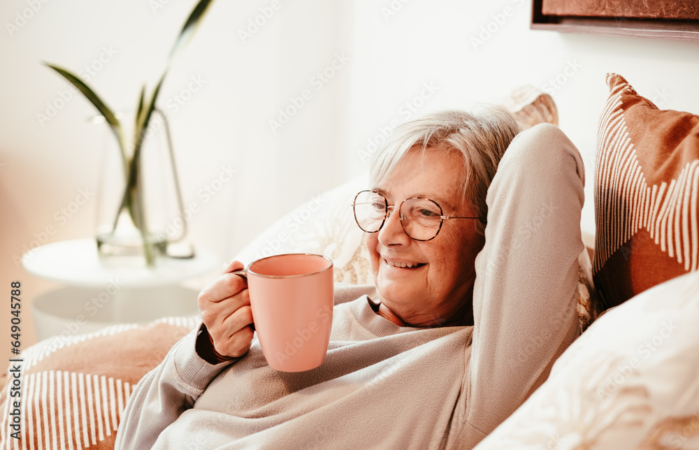 Portrait of happy relaxed handsome senior woman in bed holding a coffee cup, retirement lifestyle Portrait of happy relaxed handsome senior woman in bed holding a coffee cup, retirement lifestyle