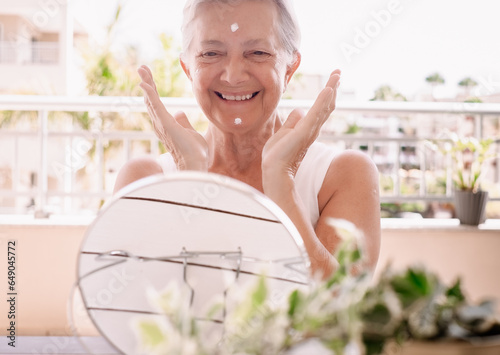 Portrait of a pretty gray-haired elderly senior woman applying anti-aging cream on her wrinkled face: take care of your skin concept