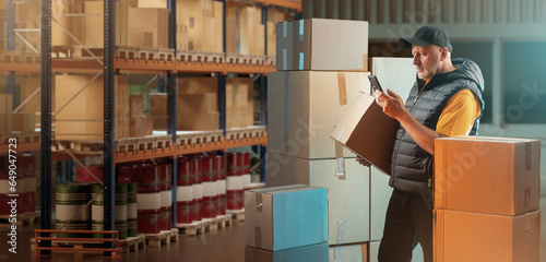 Man in customs warehouse. Storehouse worker with box. Customs officer in storage. Guy with phone and cardboard box. Man controls goods crossing border. Warehouse worker near pallet racks