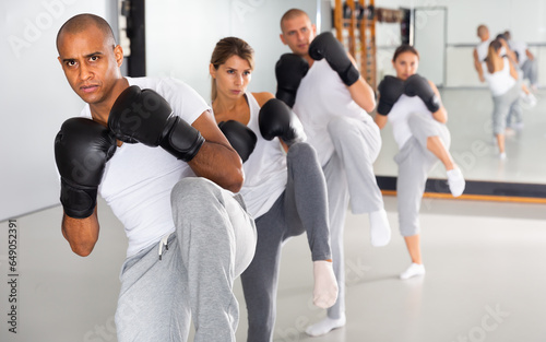 Confident hispanic male wearing boxing gloves in group workout time in self-defense in gym