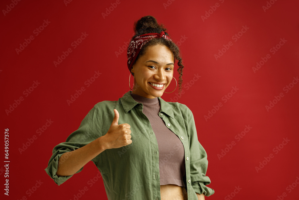 Happy woman showing thumb up with smile while standing over red studio background