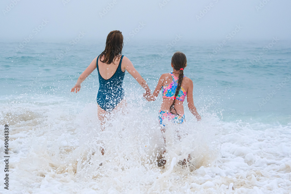 Mother and children playing on the ocean beach. Family enjoying the ocean. Mother holds girls's hands and they all look at the ocean together. Mother and children playing on the ocean beach. Family enjoying the ocean. Mother holds girls's hands and they all look at the ocean together.