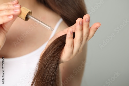 Woman applying essential oil onto hair on grey background, closeup